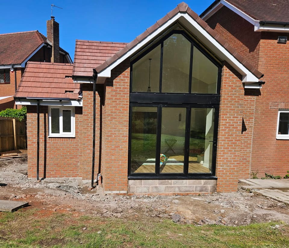 Red brick gabled extension with full-height black-framed glazing between two brick piers.