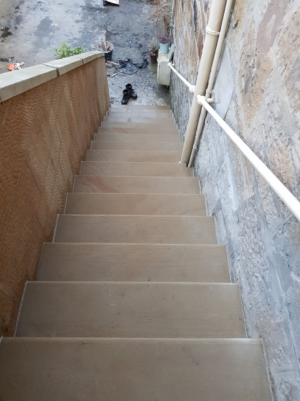 Flight of new buff sandstone steps between a tooled stone wall and an older rubble wall with a handrail.
