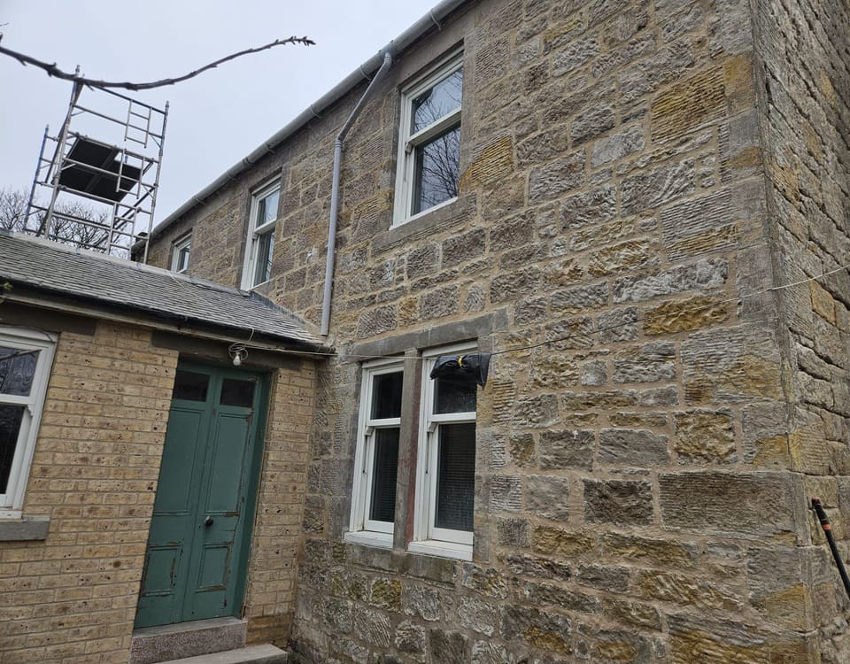 Cleaned and repointed sandstone wall beside a buff brick porch, with dressed window margins and quoins.