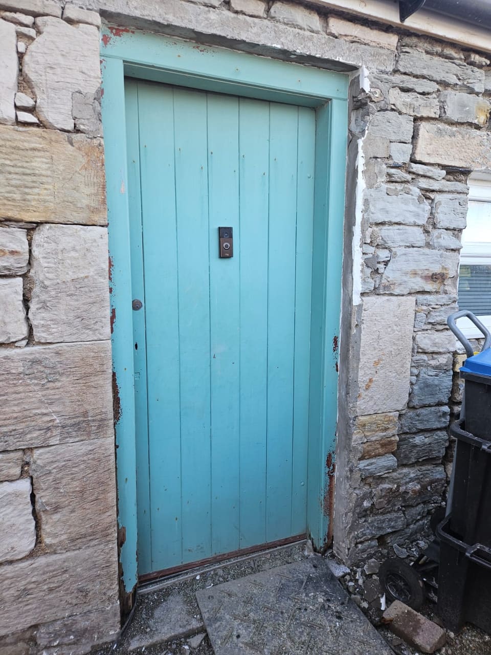 Blue-green boarded door set straight into a rubble wall, with no rybats.