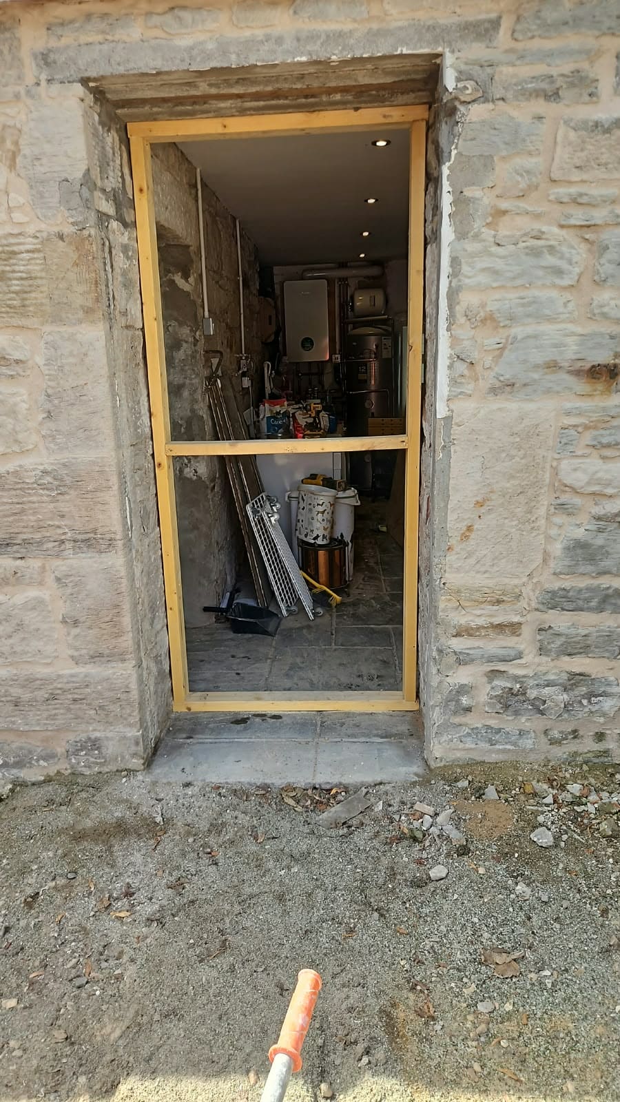 Doorway with the door removed and a timber frame in the opening for sheeting it up, the old stone running right up to the edge.