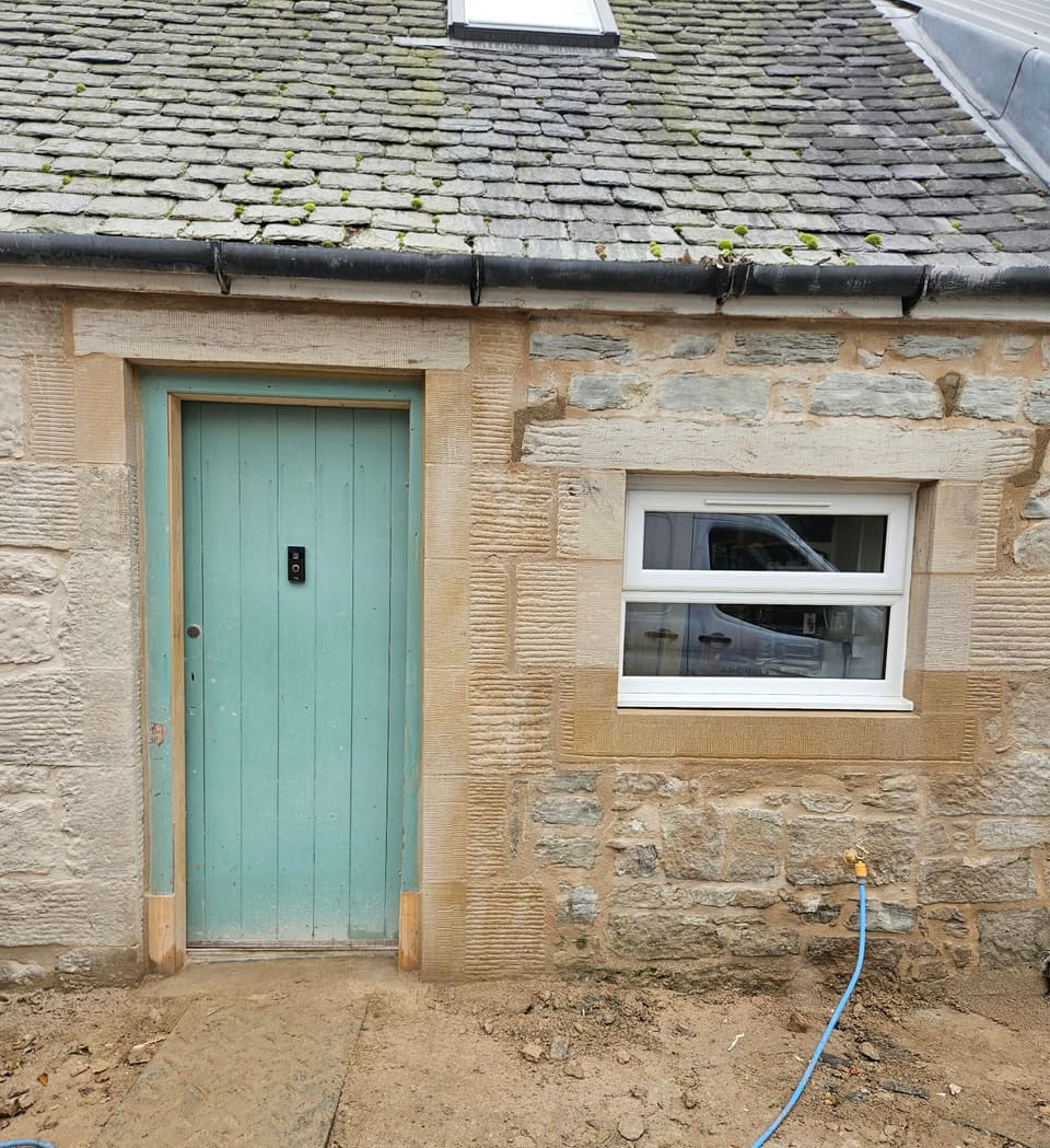 Blue-green door and a small window, both framed in dressed buff sandstone.