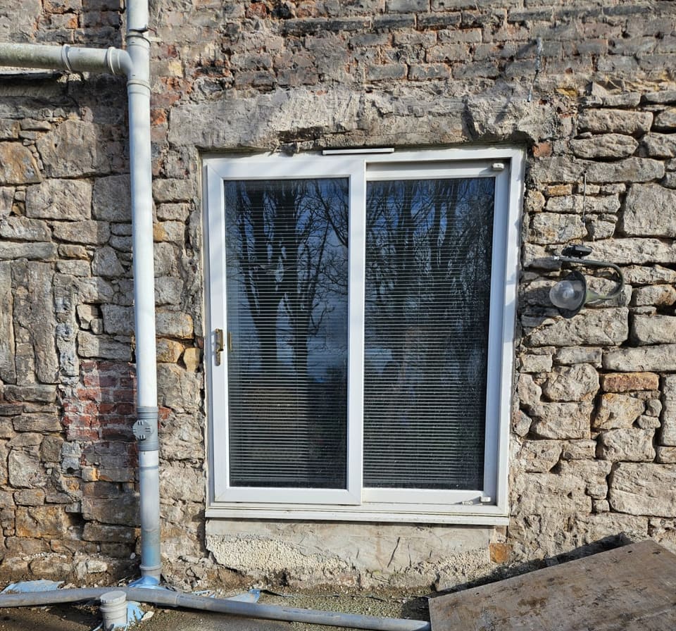 White sliding door in a rubble stone gable wall, a downpipe to its left.