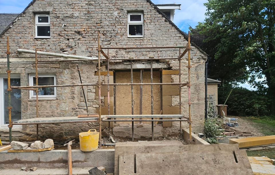 Two-storey stone gable with a scaffold round a wide new ground-floor opening framed in sandstone rybats.
