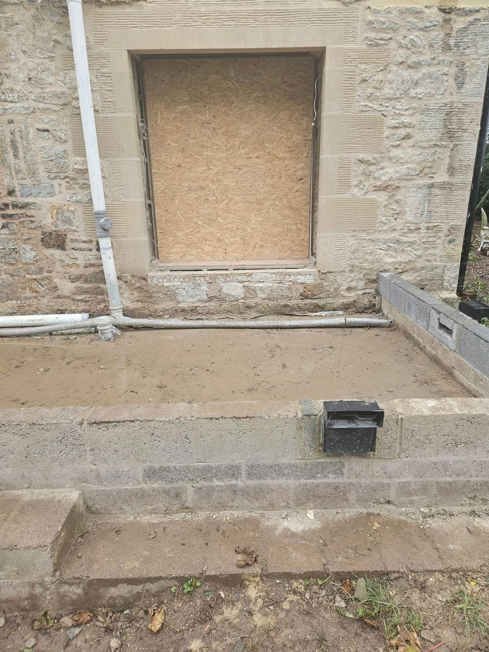 Wide opening boarded with OSB, framed by new sandstone rybats and a long lintel in a rubble gable wall.