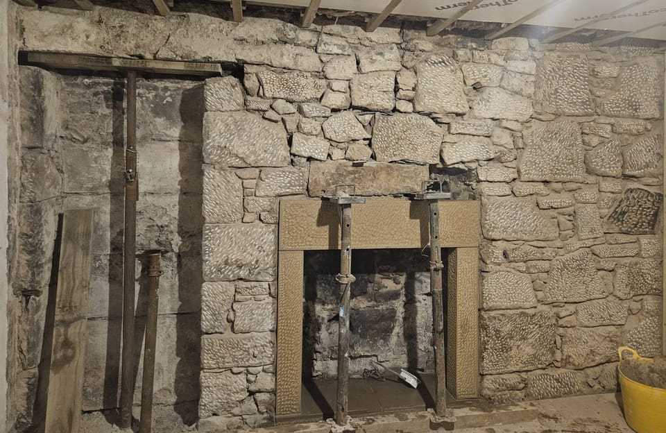 Rubble stone wall taken back to the stone, a new sandstone fireplace surround with its lintel on two adjustable props, and the recess head to the left propped too.