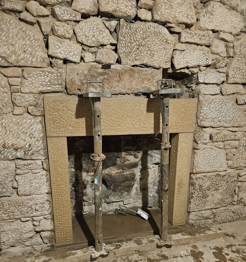 New dressed sandstone lintel and side stones set into the stone wall, the lintel held on two adjustable steel props, the old firebox behind.