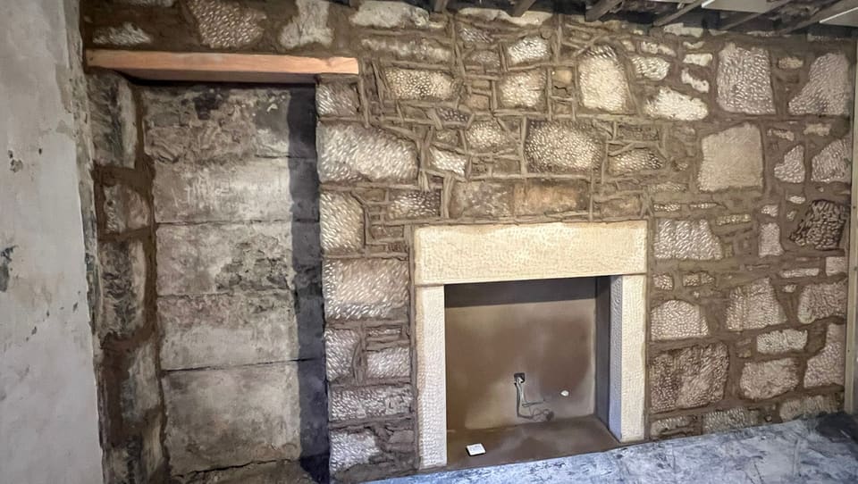 The whole rubble stone wall freshly pointed around the new sandstone fireplace surround, a new timber lintel over the recess to the left.