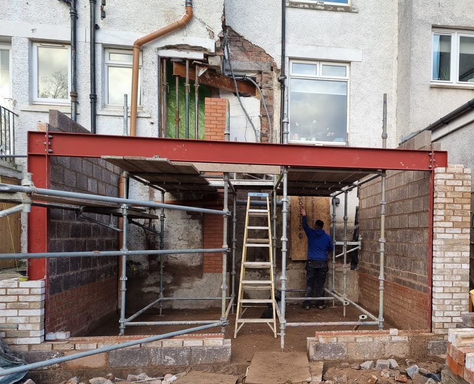 Blockwork extension shell with a red steel frame across the front and needles and props over an opening above.