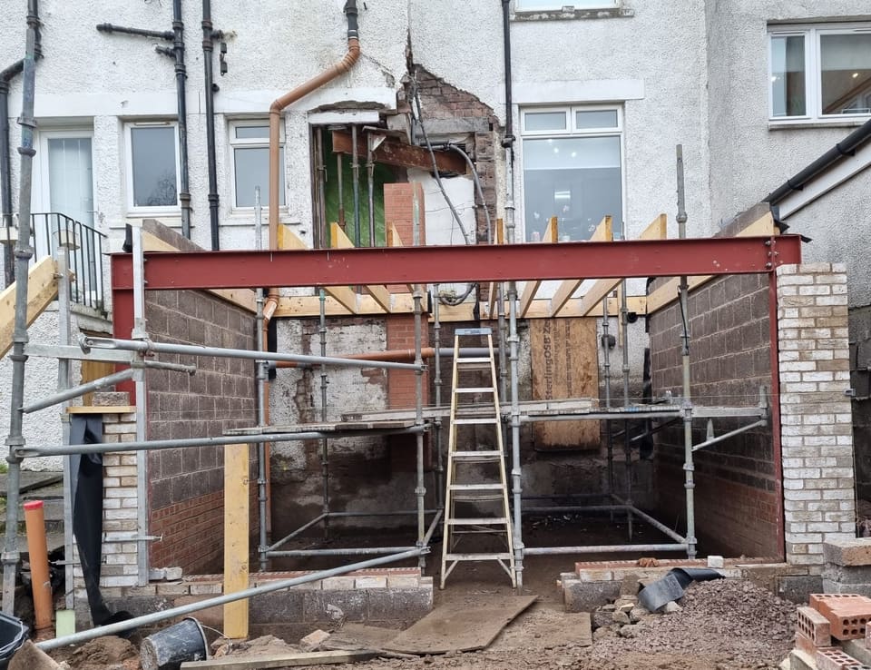 Extension shell with timber joists sitting on a red steel beam between buff brick piers.