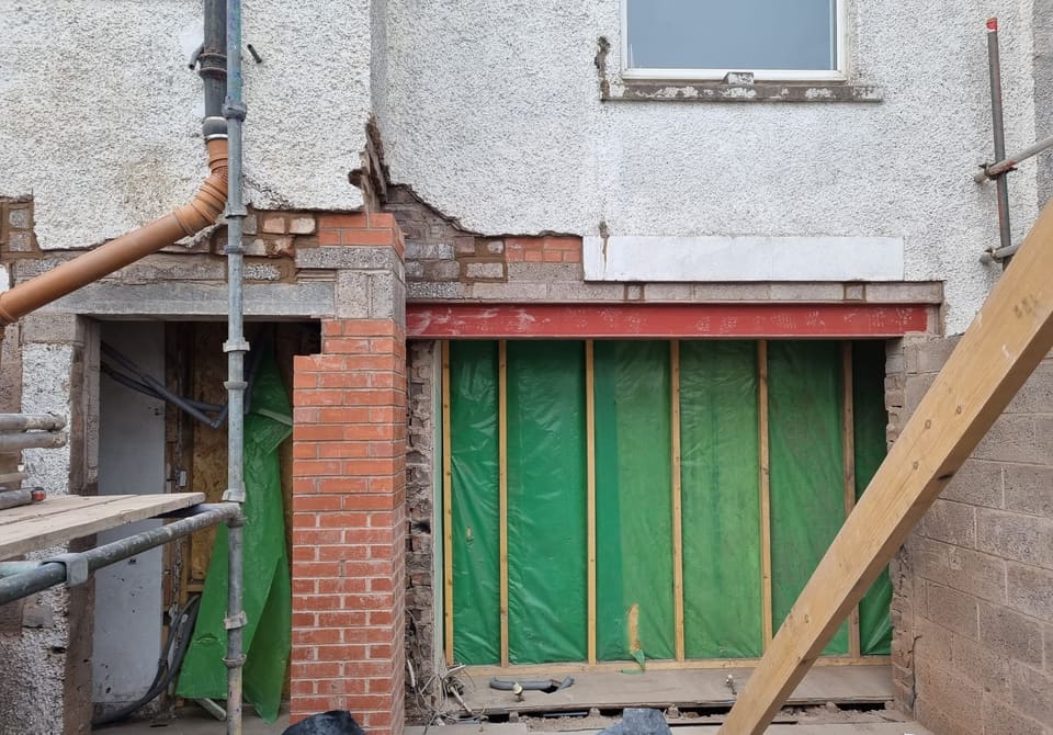 Red steel beam carrying the wall over a wide new opening, with a new red brick pier to the left.